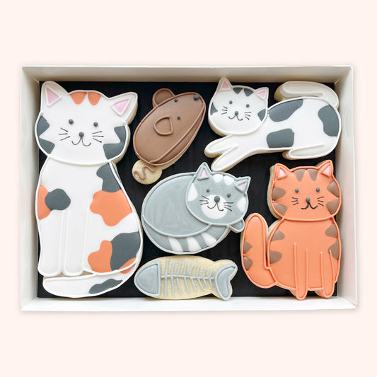 Hand-iced biscuits in a white gift box, featuring four cats in calico, grey, ginger and black-and-white designs, a brown mouse and a fish skeleton.”
