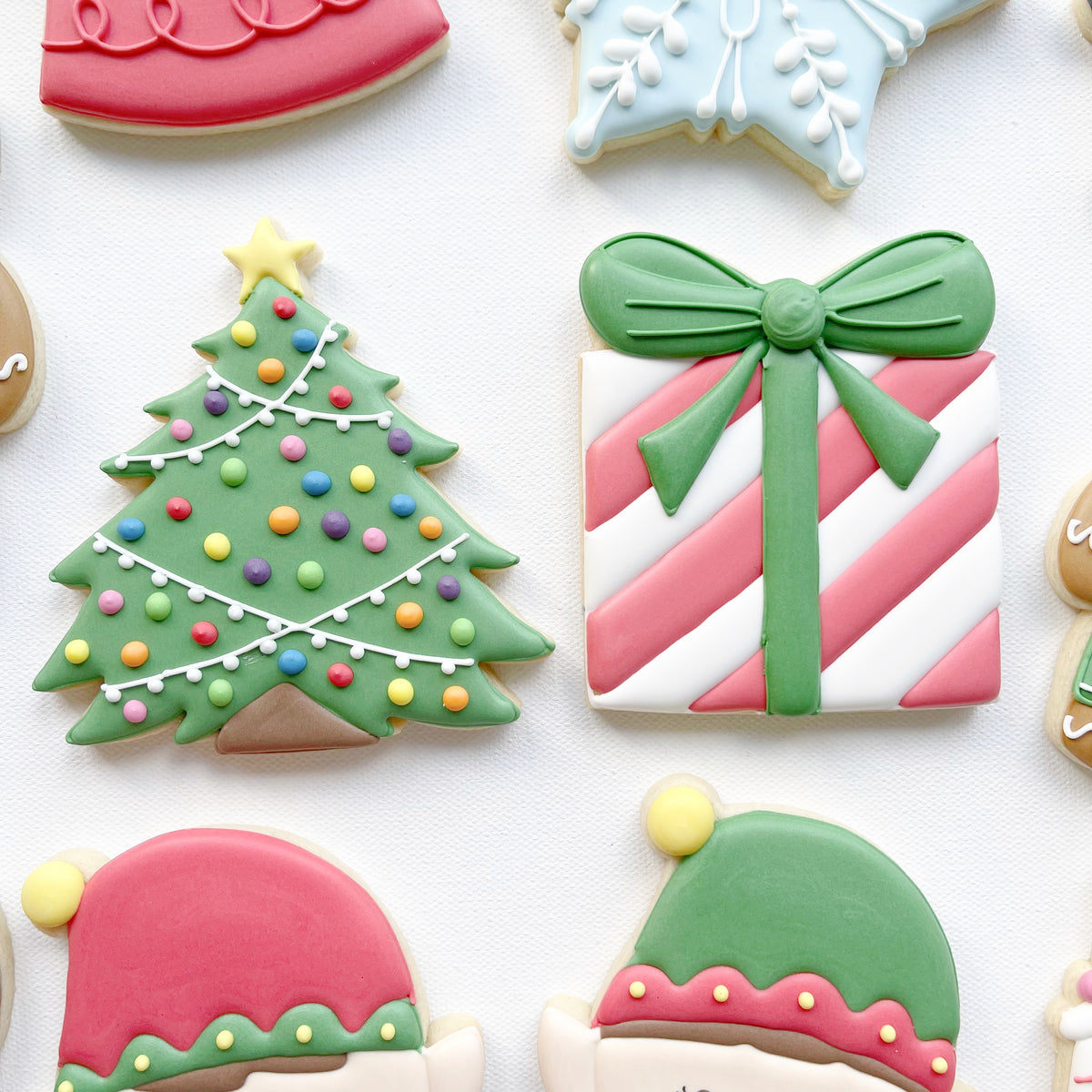 Green Christmas tree biscuit decorated with colourful baubles beside a pink-and-white striped present biscuit with a green ribbon and bow.