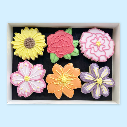 Six hand-iced flower biscuits in a white gift box, featuring a yellow sunflower, red rose and pink, orange and purple blooms