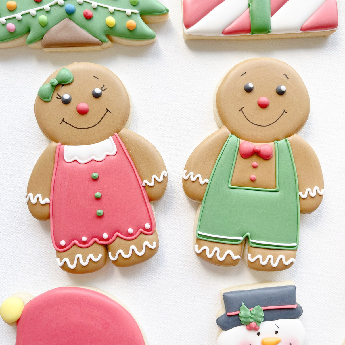 Hand-iced biscuits shaped as a gingerbread girl in a pink dress and a gingerbread boy in green dungarees with a pink bow tie.
