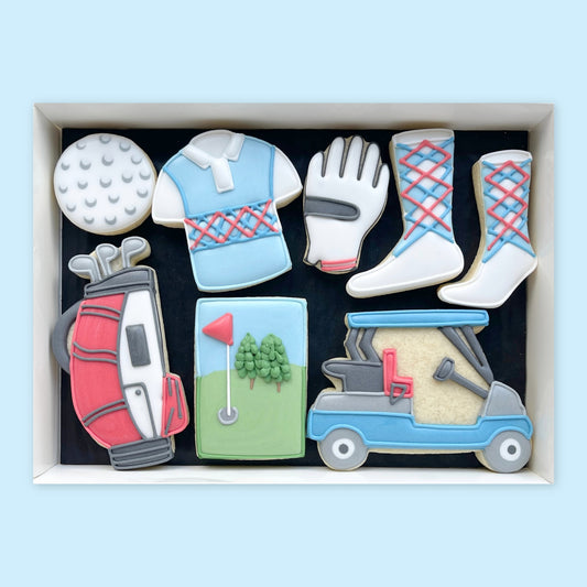 Gift box of golf-themed iced biscuits shaped as a golf ball, shirt, glove, socks, golf bag, putting green and blue golf buggy