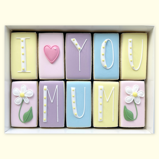 Ten pastel iced biscuits in a white gift box, arranged to read ‘I love you Mum’ using white lettering, a pink heart and two white flower designs