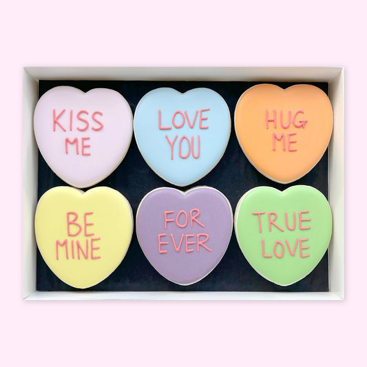 Six pastel heart-shaped iced biscuits in a white gift box, reading ‘Kiss Me’, ‘Love You’, ‘Hug Me’, ‘Be Mine’, ‘For Ever’ and ‘True Love’