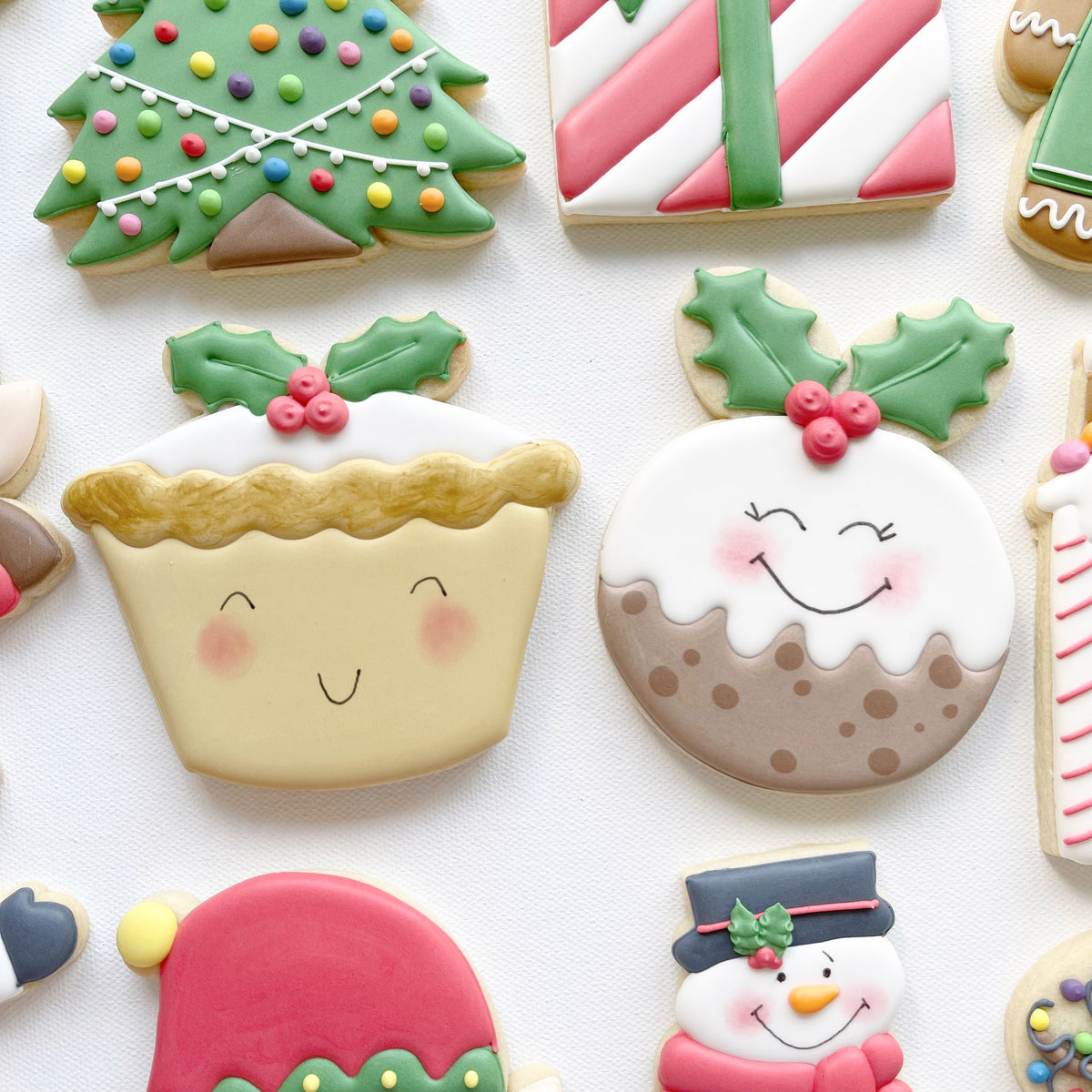 Smiling mince pie and Christmas pudding biscuit designs decorated with white icing, green holly leaves and red berries.