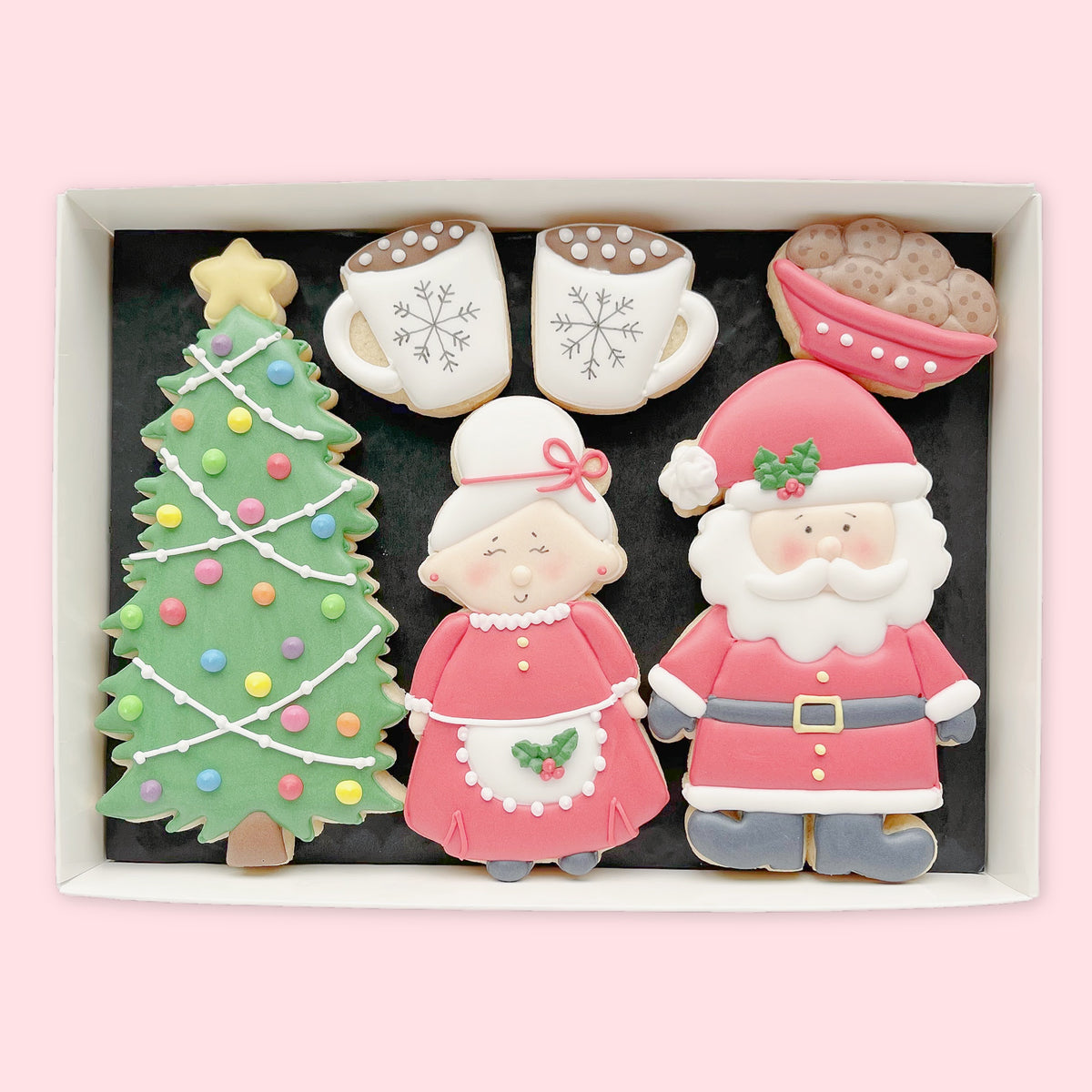 Hand-iced biscuits shaped as Mr and Mrs Claus, a Christmas tree, two hot chocolate mugs and a bowl of biscuits in a white gift box.