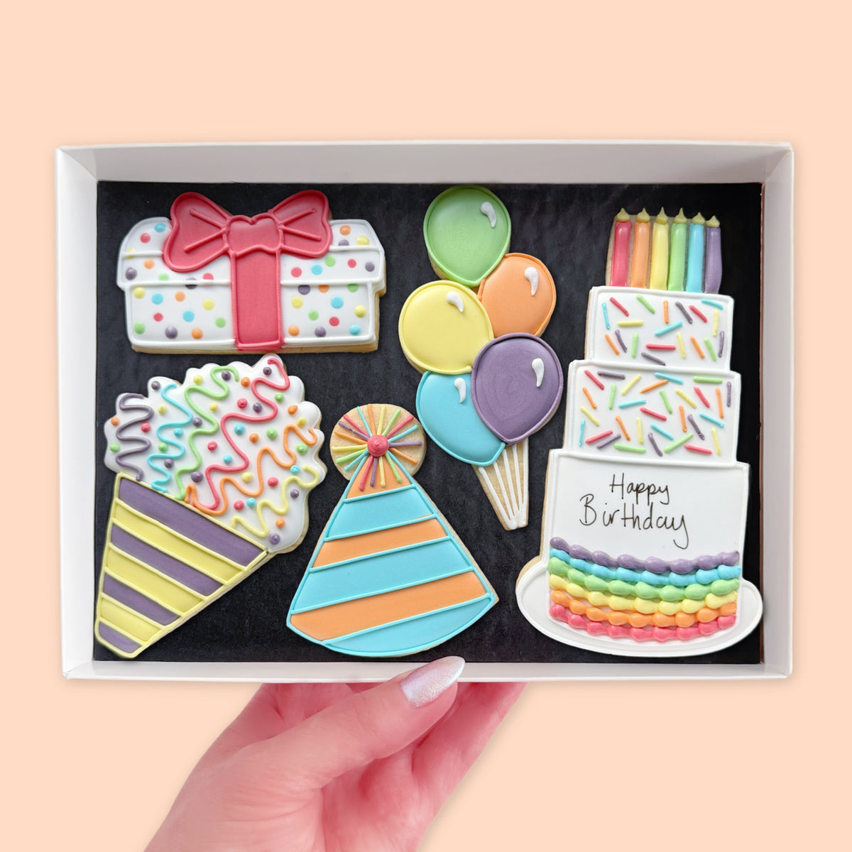 Hand holding a white gift box containing five colourful birthday iced biscuits