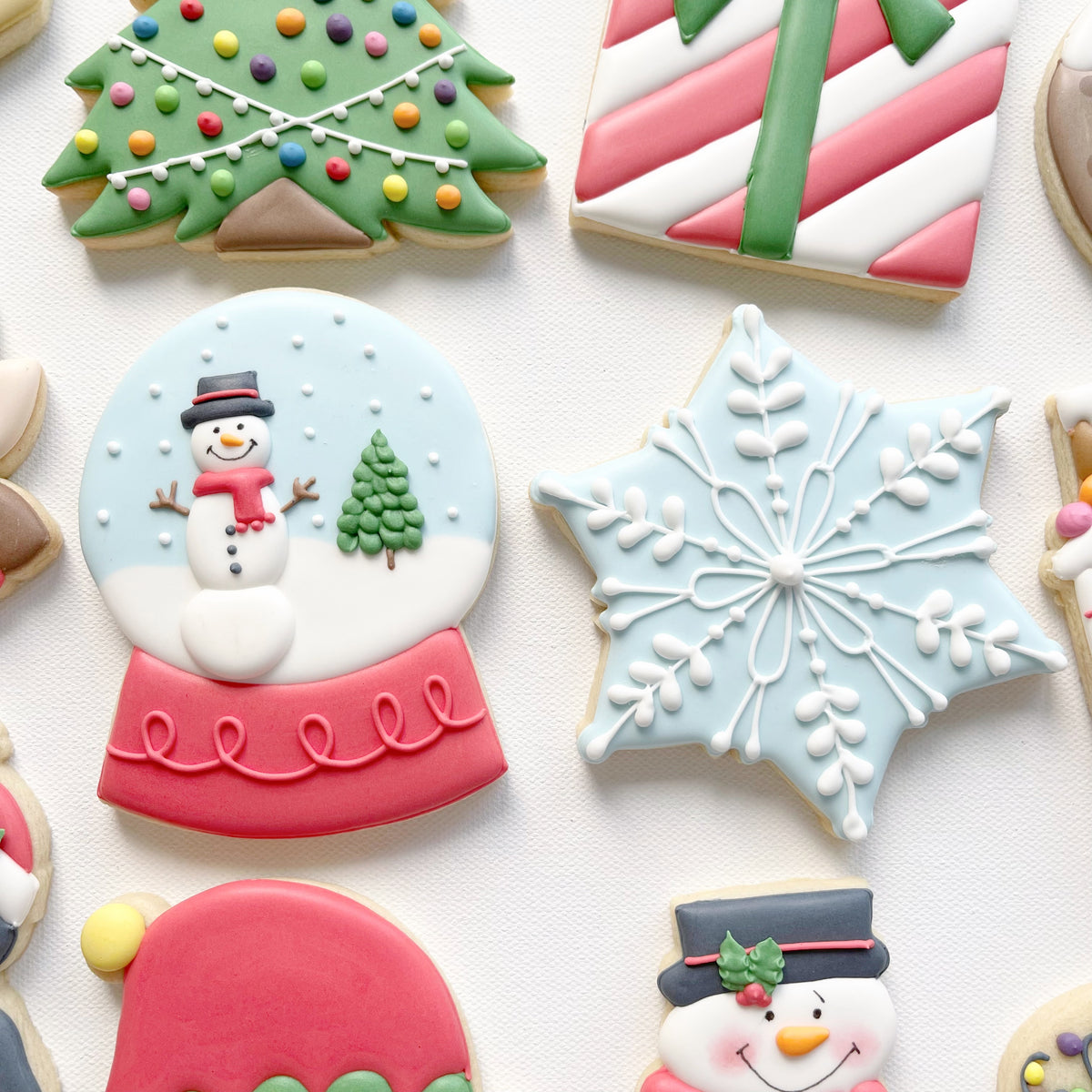 Close-up of a snow globe biscuit featuring a snowman and Christmas tree beside a pale blue snowflake biscuit with white icing details.