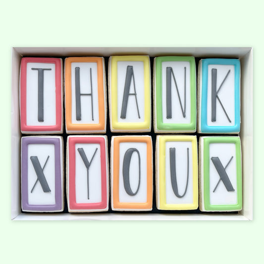 Ten rectangular iced biscuits with colourful borders and black letters spelling ‘THANK X YOU X’, arranged in a white gift box.