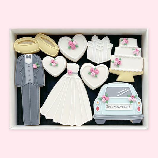 Gift box of wedding-themed iced biscuits shaped as rings, a suit, wedding dress, hearts, gift, cake and a car with ‘Just Married’ lettering