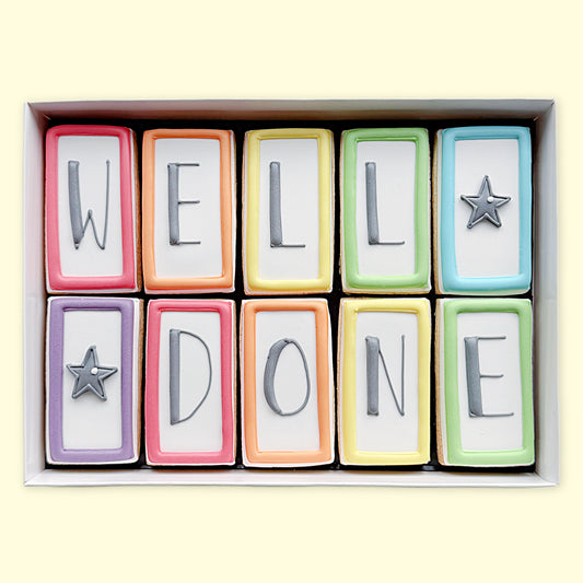 Ten rectangular iced biscuits with colourful borders, grey letters spelling ‘WELL DONE’ and two star designs, arranged in a white gift box.