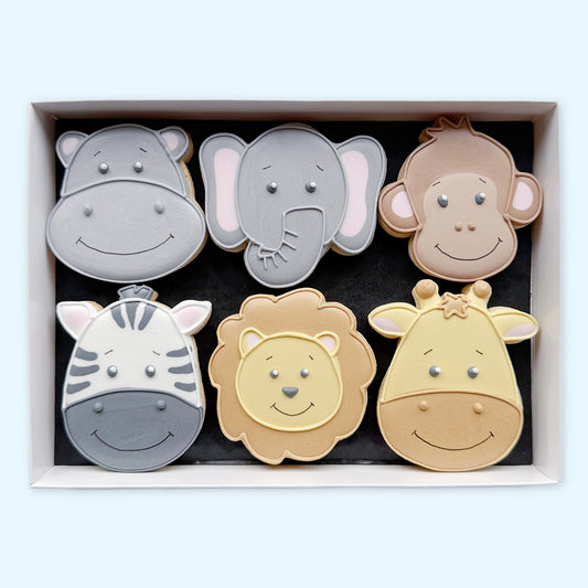 Six hand-iced animal-face biscuits in a white gift box, featuring a smiling hippo, elephant, monkey, zebra, lion and giraffe