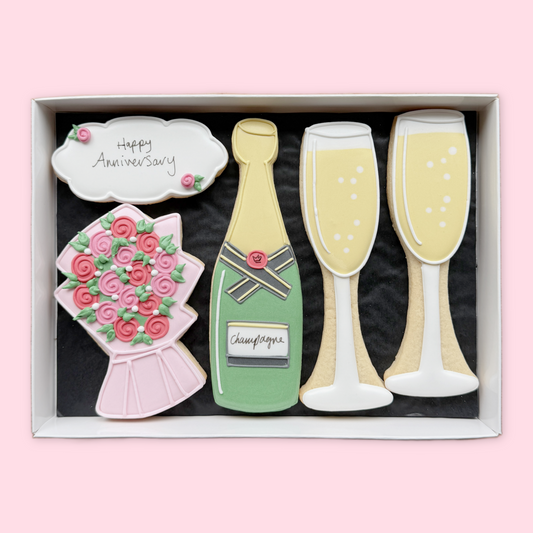 Hand-iced anniversary biscuits in a white gift box, featuring a champagne bottle, two glasses, flowers and a Happy Anniversary plaque