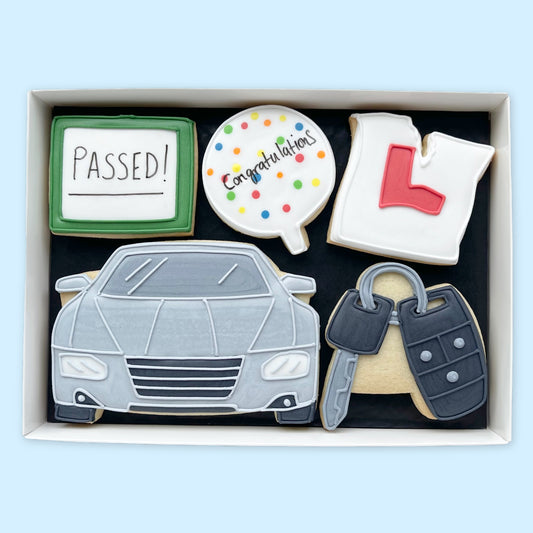 Hand-iced biscuits in a white gift box, featuring a grey car, car keys, torn L plate, ‘Passed!’ plaque and ‘Congratulations’ balloon.