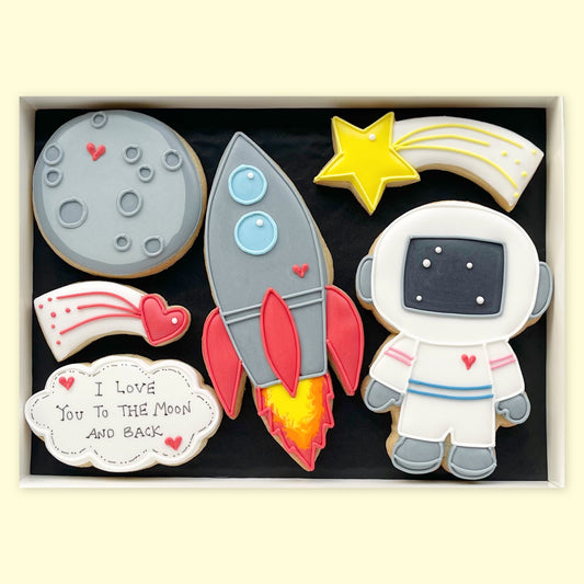 Hand-iced space biscuits in a white gift box, featuring an astronaut, rocket, moon, shooting star, heart and ‘I love you to the moon and back’ plaque.”