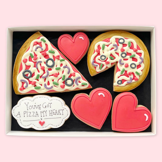 Hand-iced biscuits in a white gift box, featuring a pizza slice, a pizza with a slice missing, three red hearts and a ‘You’ve got a pizza my heart’ plaque.