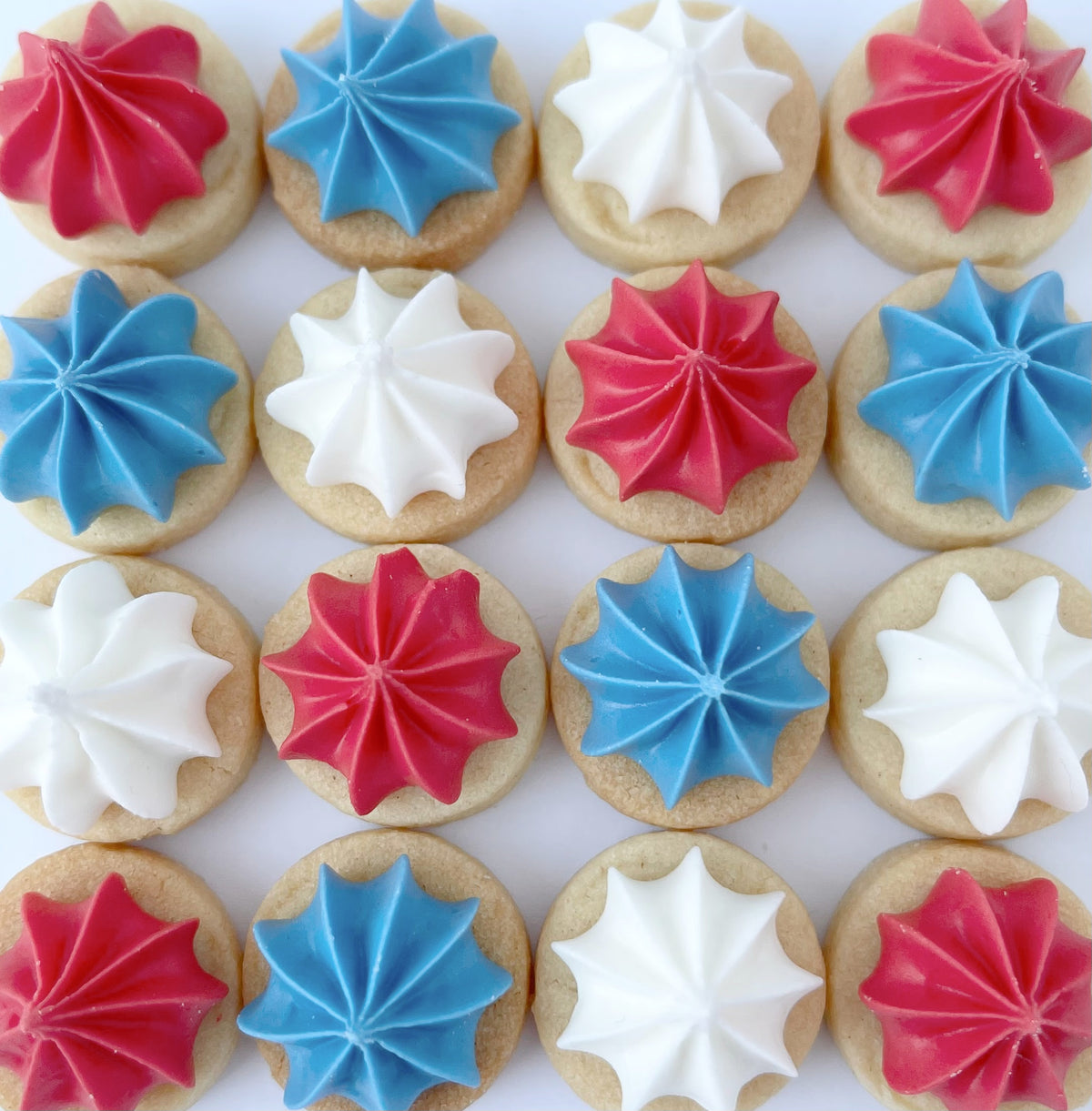 Mini biscuit gems arranged in neat rows on a white background, topped with alternating red, white and blue piped icing.